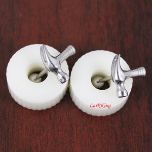 May include: A pair of silver hammer earrings with a white background. The earrings are small and have a simple design.