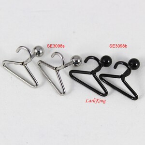 May include: Two pairs of earrings featuring a small hanger design. One pair is silver with a silver ball, and the other pair is black with a black ball. The earrings are labeled "SE3098s" and "SE3098b".