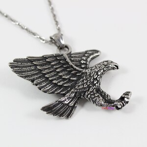 May include: A silver eagle pendant necklace with a detailed design. The eagle is in flight with its wings spread wide. The pendant is attached to a silver chain.