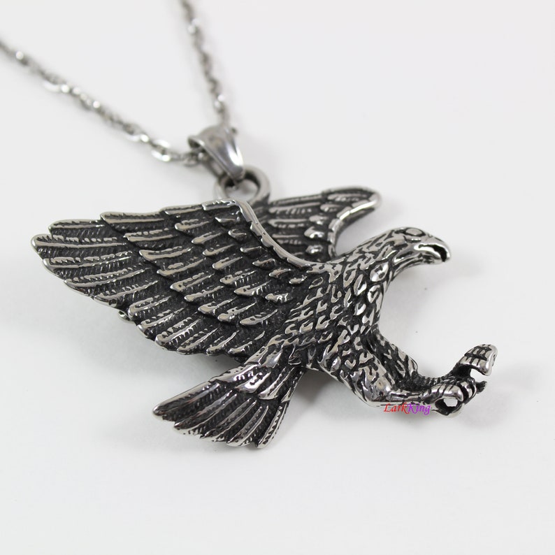 May include: A silver eagle pendant necklace with a detailed design. The eagle is in flight with its wings spread wide. The pendant is attached to a silver chain.
