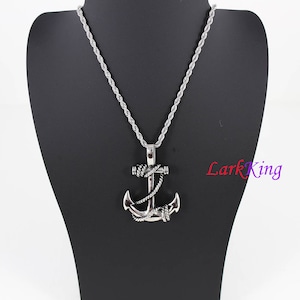 May include: A silver anchor pendant necklace with a rope design. The necklace is on a silver rope chain.
