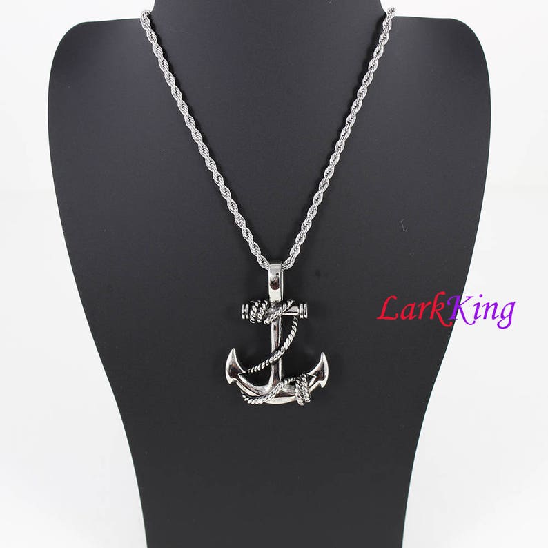 May include: A silver anchor pendant necklace with a rope design. The necklace is on a silver rope chain.