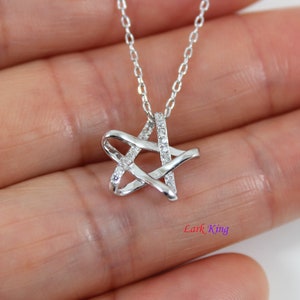 Puede incluir: Un collar con colgante en forma de estrella plateada que presenta una cadena delicada y una estrella con un lado incrustado de peque&ntilde;as piedras claras. El texto Lark King es visible en la esquina inferior derecha de la imagen.