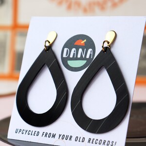 Black recycled vinyl record teardrop earrings dangling from small metallic teardrop posts on a card that has the DANA Jewelry logo.