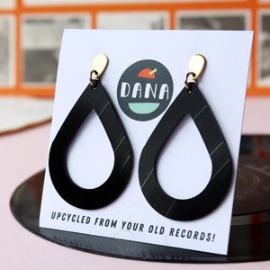 Black recycled vinyl record teardrop earrings dangling from small metallic teardrop posts on a card that has the DANA Jewelry logo.