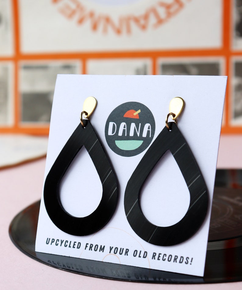 Black recycled vinyl record teardrop earrings dangling from small metallic teardrop posts on a card that has the DANA Jewelry logo.
