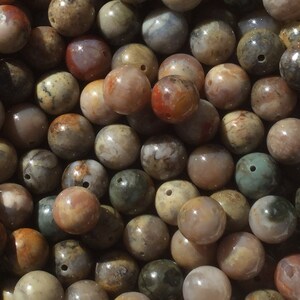 May include: A close-up of a collection of round, multi-colored agate beads. The beads are a mix of brown, white, gray, and red colors with intricate patterns.