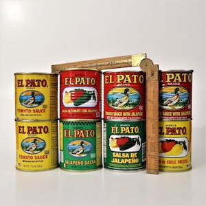 May include: A collection of eight red, green, and yellow cans of El Pato brand tomato sauce and jalapeno salsa. The cans are arranged in two rows of four. The cans are all the same size and shape, and they all have the same logo. The logo features a duck with a red beak and a yellow body. The cans are all labeled with the brand name, the product name, and the net weight.