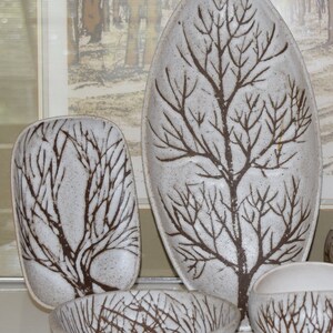 May include: Set of four white ceramic serving dishes with a brown tree branch design. The dishes are oval and round in shape.