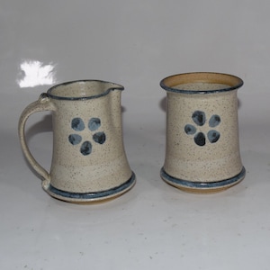 May include: Two ceramic pieces with a speckled white glaze and blue floral designs. A pitcher with a handle and a shorter, cylindrical cup.