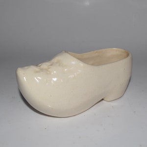 May include: A white ceramic clog-shaped planter. The planter is glazed and has a smooth finish.