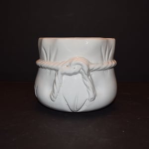 May include: White ceramic planter shaped like a bag with a rope tied around it.