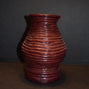 May include: A dark brown ceramic vase with a textured, ribbed design. The vase is tall and narrow with a rounded base.