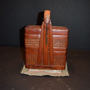 May include: A wooden box with a woven lid and a handle. The box is sitting on a patterned fabric.
