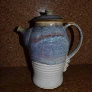 May include: A blue and white ceramic teapot with a brown lid and a handle. The teapot has a glazed finish and a textured design.