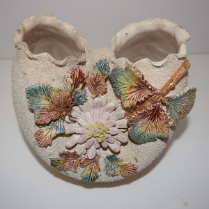 May include: A white ceramic vase with two openings, decorated with raised floral and leaf designs in shades of brown, green, and pink.