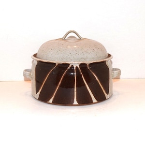 May include: A ceramic cooking pot with a lid. The pot is primarily brown with white vertical stripes radiating from the center. The lid and handles are a speckled off-white color. The pot has two side handles and a loop handle on the lid.