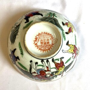 May include: A ceramic bowl with a crackle glaze finish featuring colorful hand-painted figures and landscape elements. The base includes a red stamp reading ORIENTAL OBJECTS D'ART, MADE IN MACAO, and NOT FOR FOOD USE, along with Chinese characters.