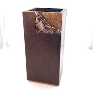 May include: A dark brown rectangular vase with a decorative gold and brown accent on the side. The accent features a grid pattern and a textured appearance. The vase has a square opening and a dark interior.