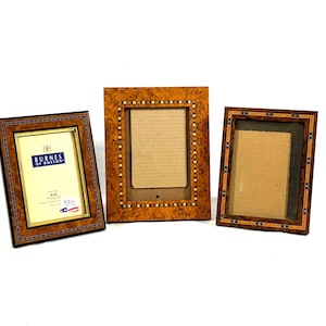 May include: Three decorative wooden picture frames. The frames have a brown and gold color scheme with intricate inlaid designs. One frame has a label that reads "Burnes of Boston" and is sized for a 4x6 inch photo.
