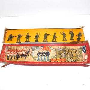 May include: Vintage toy soldier set in a worn cardboard box. The box features illustrations of soldiers, flags, and military scenes. The set includes small green plastic toy soldiers in various poses.