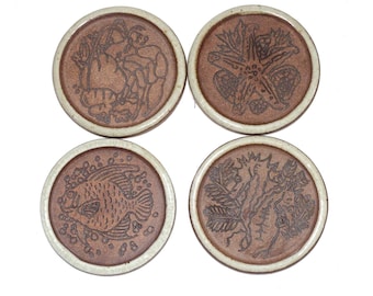 May include: Four brown ceramic coasters with off-white rims. Each coaster features a different embossed design: a figure with a sack, a starfish, a fish, and a botanical illustration. The coasters are arranged on a white background.