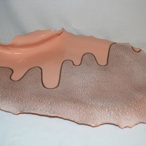 May include: A ceramic serving dish with an irregular shape and a brown speckled glaze. The dish has a pink glaze that drips down the sides, creating a unique design.
