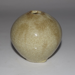 May include: A small, round, ceramic vase with a speckled, tan exterior. The vase has a narrow opening at the top and a slightly rounded base. The surface has a glossy finish. The overall shape is spherical.
