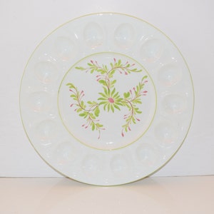 May include: White ceramic egg plate with 12 individual indentations around the edge. The center of the plate features a hand-painted design of green leaves and pink flowers.