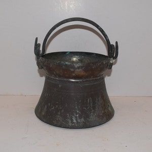 May include: An antique copper pot with a metal handle. The pot has a dark patina and is slightly tarnished.