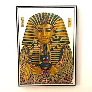 May include: A framed print of an Egyptian pharaoh, featuring a gold headdress with blue stripes, a gold face, and a detailed collar. The pharaoh holds a crook and flail. The artwork is set against a white background.