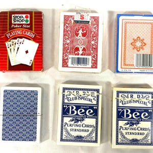 Puede incluir: Una variedad de barajas de cartas. Las barajas son de varios colores, incluyendo rojo, azul y blanco. Algunas barajas tienen texto que dice "STOP SHOP Poker Size PLAYING CARDS" y "Bee PLAYING CARDS STANDARD".