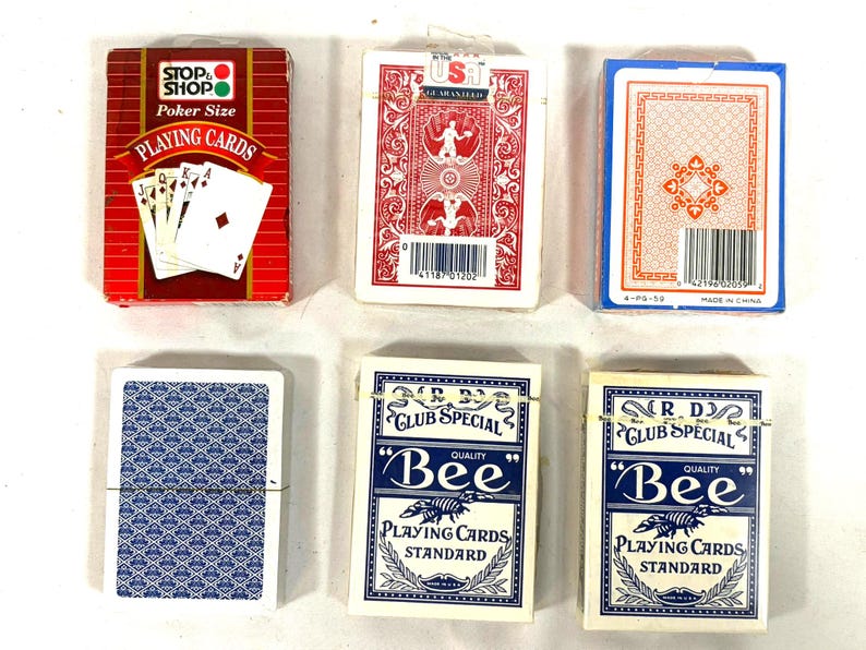 Puede incluir: Una variedad de barajas de cartas. Las barajas son de varios colores, incluyendo rojo, azul y blanco. Algunas barajas tienen texto que dice "STOP SHOP Poker Size PLAYING CARDS" y "Bee PLAYING CARDS STANDARD".
