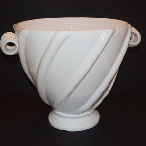 May include: A large white ceramic bowl with two twisted handles. The bowl has a swirling design and a wide, round base.