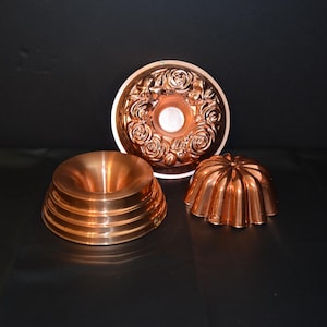 May include: Three copper cake molds. One is a round mold with a rose design, another is a round mold with a fluted design, and the third is a round mold with a ridged design.