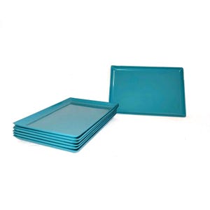 May include: A stack of six rectangular turquoise serving trays, with a seventh tray positioned separately. The trays have a glossy finish and are arranged against a white background. These trays are suitable for serving food.