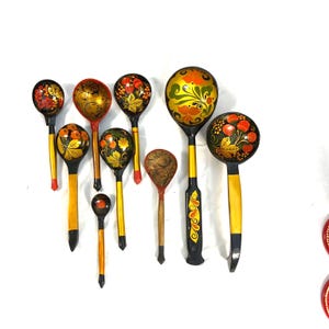 May include: A collection of hand-painted wooden spoons with intricate floral designs. The spoons feature a variety of colors, including red, yellow, and black, and are arranged on a white background. The spoons vary in size and shape.