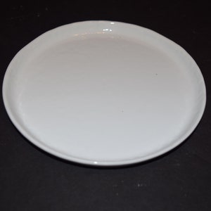 May include: A plain white ceramic plate with a slightly raised rim.