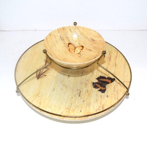 May include: A two-tiered serving set with a light beige, wood-grain pattern. The top tier is a small bowl with a butterfly design, held by a gold-colored metal stand. The bottom tier is a large, round plate with a butterfly design.
