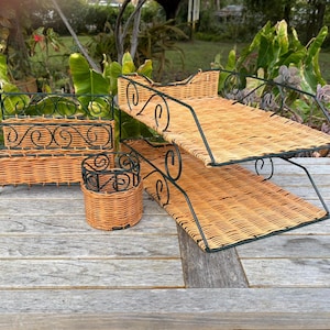 May include: A collection of vintage wicker serving trays and a small basket. The trays have a woven design with black metal scrollwork frames. The small basket has a similar design. The items are displayed on a weathered wooden surface.