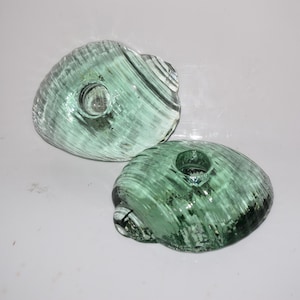 Puede incluir: Dos portavelas de vidrio verde con forma de conchas marinas. Los portavelas tienen una superficie texturizada y un pequeño agujero en el centro para una vela.
