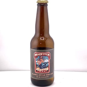 May include: A brown glass bottle of Seawitch Denali Red Alaska Style Red Ale. The label features a mermaid illustration and the text "Seawitch Denali Red Alaska Style Red Ale". The bottle is 12 fl oz and 5.3% alcohol.