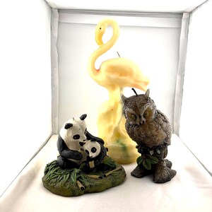 May include: A collection of decorative figurines, including a tall yellow flamingo, a brown owl perched on a branch, and a panda family. The panda family is black and white, sitting on a green base. The owl has green eyes.