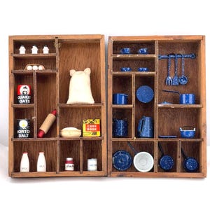 May include: Wooden display case with miniature kitchen items. Includes blue speckled cookware, utensils, and food items like oats, salt, and a cookbook. A rolling pin and milk bottles are also visible.