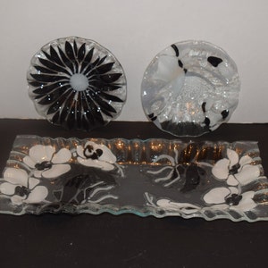 May include: Three glass serving dishes with black and white floral designs. The dishes are made of clear glass with a wavy edge. The designs are painted on the glass and are visible from both sides.