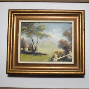 Op de afbeelding: Een ingelijst landschapsschilderij in olieverf met een serene sc&egrave;ne met bomen, rotsen en een brug. Het kunstwerk is gevat in een goudkleurige lijst, wat de vintage esthetiek versterkt. Het schilderij toont een mix van groene, oranje en blauwe tinten.