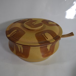 May include: A brown and tan ceramic serving dish with a lid and a matching serving spoon. The dish has a geometric pattern.