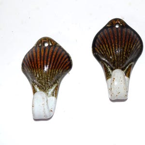 May include: Two ceramic wall hooks. Each hook has a fan-shaped top with brown and tan stripes, a dark brown border, and a white, speckled hook. A small hole is at the top for hanging.