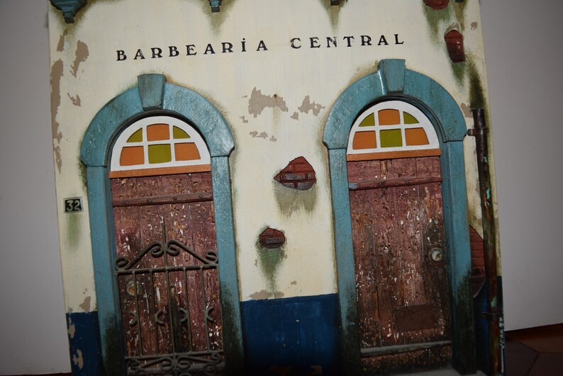 May include: A weathered building facade with two arched doorways, each with a stained glass window and a wooden door. The building is painted white with blue trim and has the words "BARBEAR&Iacute;A CENTRAL" written above the doorways.