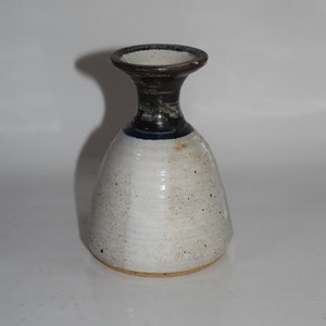 May include: A white ceramic vase with a brown and blue rim. The vase has a wide base and a narrow neck.
